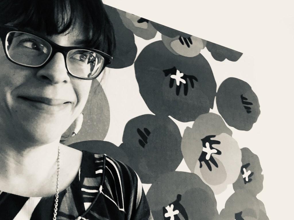 black and white photo of Jen Worick in front of a Marimekko-like canvas of large brown poppies